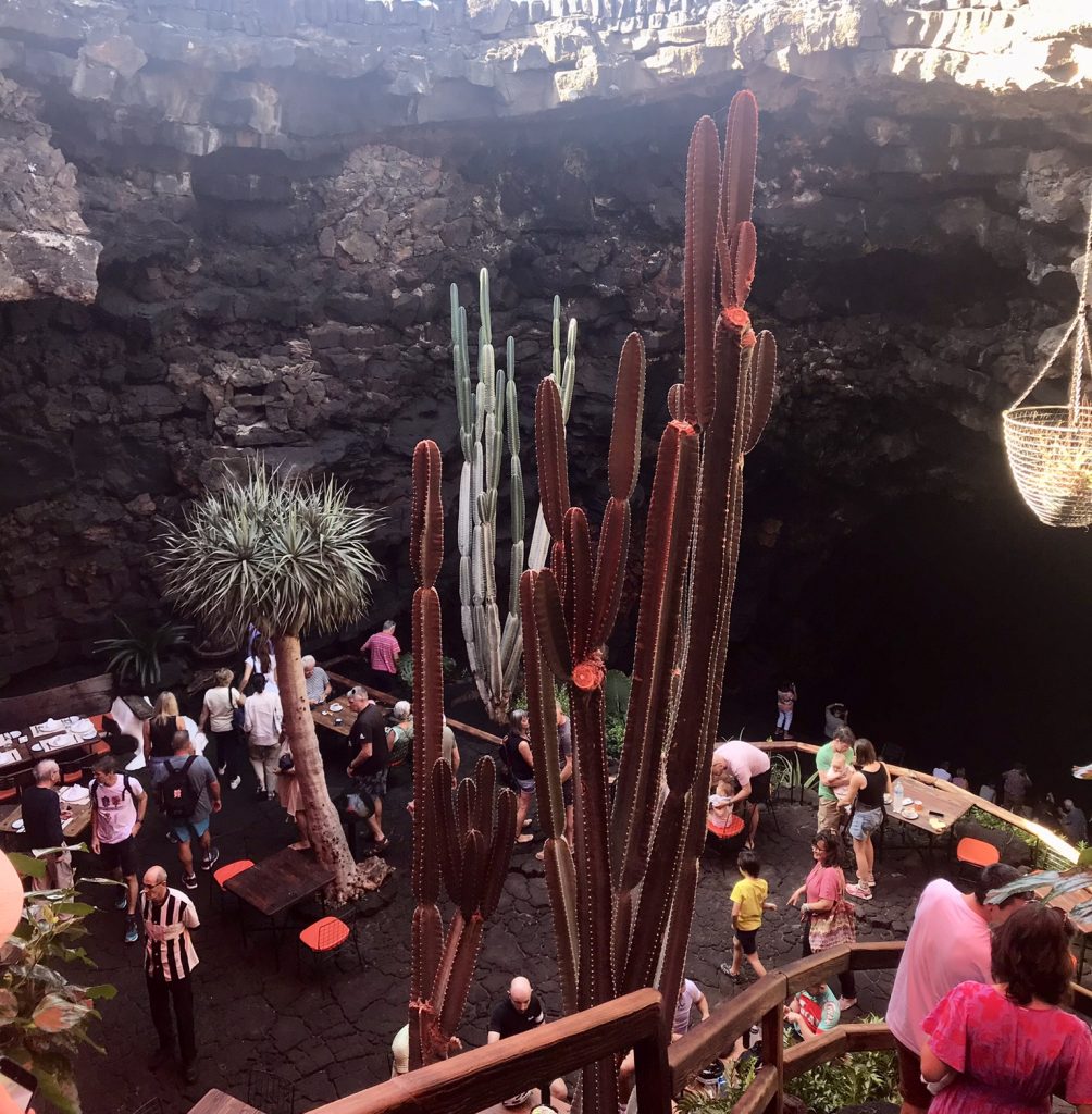 Picture of people starting to climb the starrers down into the famous Jameos del Agua, featuring tall cacti and a small restaurant